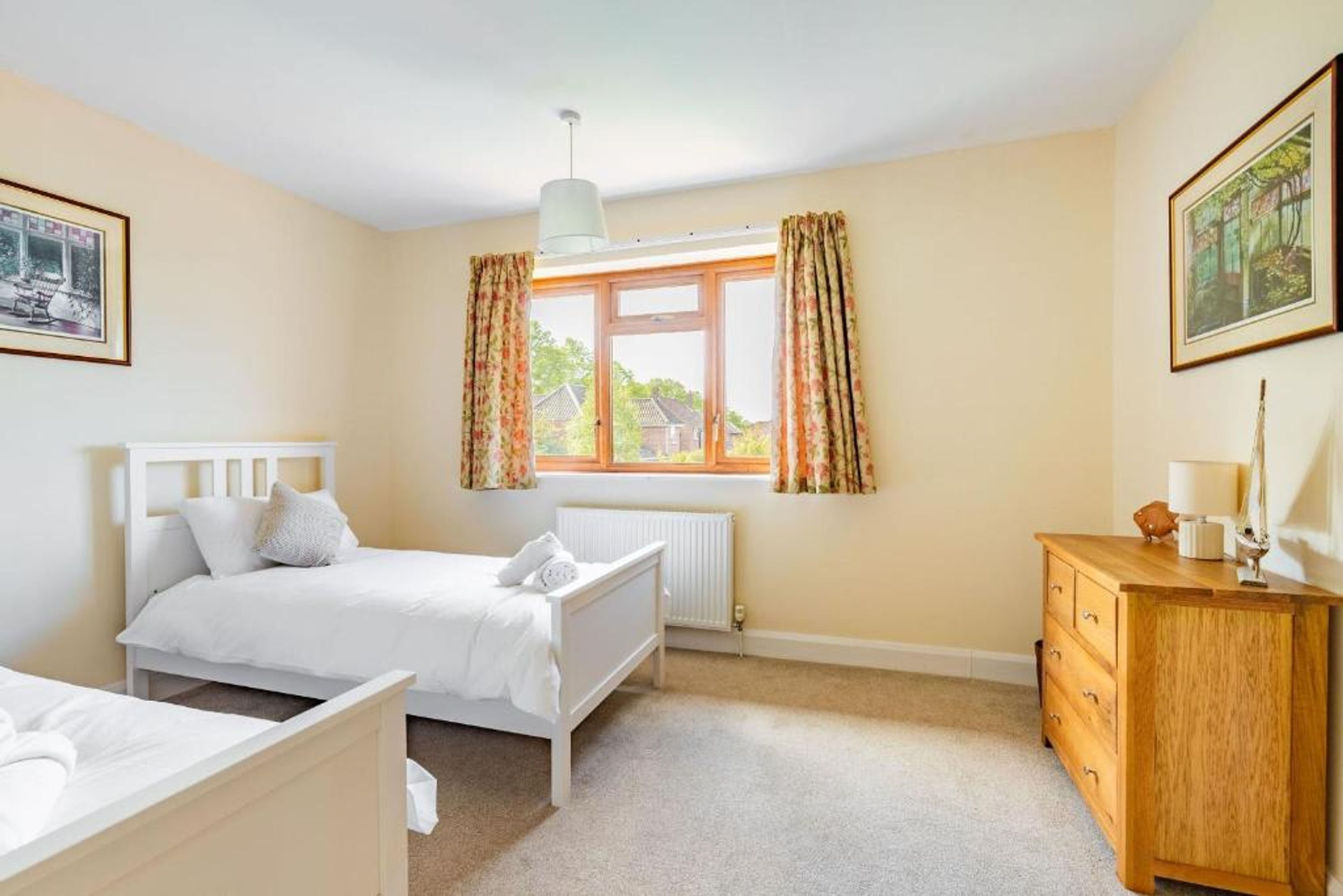 A bedroom with a bed, a dresser, a radiator, and a window with curtains.
