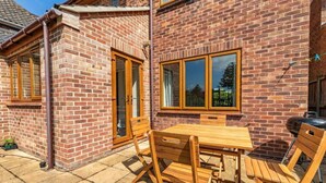 A brick house with a patio, wooden table and chairs, and a barbecue grill. - Host Stay Welsford House (Norwich)