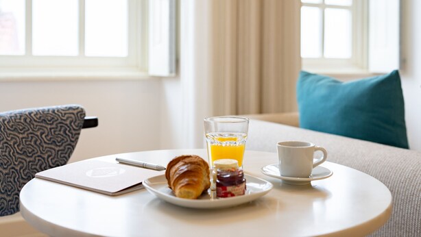 A breakfast setting with a croissant, a glass of orange juice, and a cup on a round table.