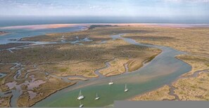 An aerial view of a coastal area with a winding river, several boats, and a distant shoreline. - Host Stay The Hideaway (Wells-next-the-Sea)