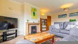 A living room with a flat-screen TV, a fireplace, a sofa, and a bookshelf. - Host Stay The Hideaway (Wells-next-the-Sea)