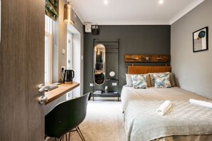 A modern hotel room with a bed, a desk, and a chair. There is a mirror and a shelf with books and a clock. - Host Stay The Old Laundry House (Norwich)