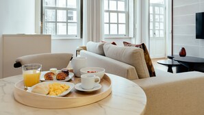 Una bandeja de desayuno con croissants, huevos revueltos y jugo de naranja sobre una mesa de mármol en una habitación de hotel con un sofá y un televisor en la pared.