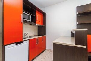 Una cocina compacta con gabinetes rojos, un lavavajillas blanco y un microondas.