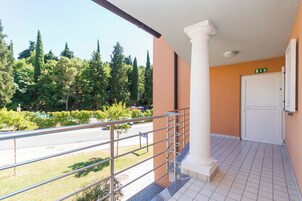 A balcony with a metal railing overlooking a parking area and trees.