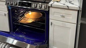 Una cocina con microondas, horno y estufa de acero inoxidable. Hay dos fregaderos, un estante para especias y un perchero para toallas.