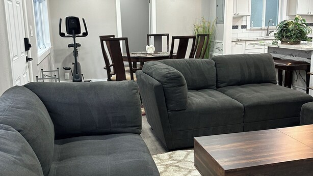 Una sala de estar moderna con dos sofás grises grandes, una mesa de centro de madera y un comedor con una mesa y sillas blancas.