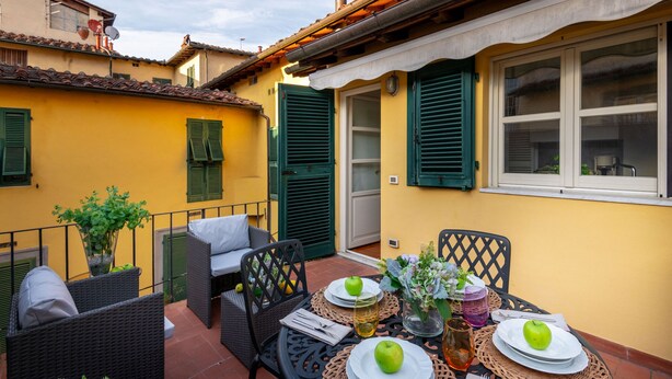 A patio with outdoor furniture, a table set with plates, apples, and drinks, and a yellow building with green shutters. - The Terrace Retreat in Lucca (Lucca)