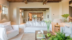 Amplia sala de estar con techo alto de madera, sofás blancos, una mesa de centro con objetos decorativos y vista al comedor.