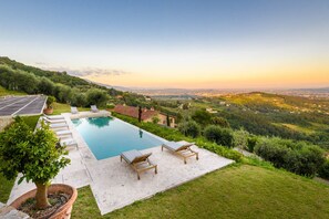 Una piscina con lettini, un albero in vaso e vista su un paesaggio collinare.