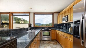 A kitchen with granite countertops, stainless steel appliances, wooden cabinets, and a stone floor.