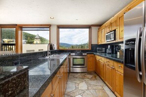 Une cuisine dotée de plans de travail en granit, d’appareils électroménagers en acier inoxydable, d’armoires en bois et d’un sol en pierre.
