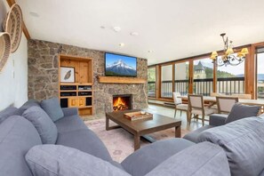 A living room with a stone fireplace, a television, and a balcony with outdoor seating.