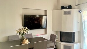A modern living room with a flat-screen TV mounted on the wall, a fireplace, and a dining area with a table and chairs. - Villa Evanthia (Avlonárion)