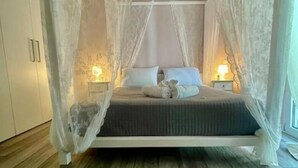 A bedroom with a canopy bed, bedside lamps, and a wooden floor. - Villa Evanthia (Avlonárion)