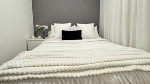 A neatly made bed with a white duvet, a bedside table with a vase of flowers, and a grey accent wall. - dubai resort (Ponteareas)