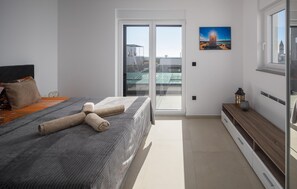 Relax in this serene bedroom with a large bed, sliding glass door to a balcony, and a framed lighthouse view.