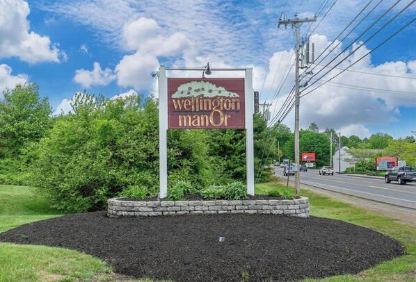 Señal de Wellington Manor con un área arbolada al frente.