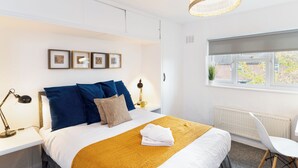 A neatly arranged bedroom with a bed, bedside tables, a chair, and a window with a view. - Terrace | Parking | Great for Couples | Sleeps 7 (Bristol)