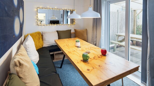 A cozy room with a wooden table, a bench with cushions, a mirror with lights, and a view of the outside. - Terrace | Parking | Great for Couples | Sleeps 7 (Bristol)