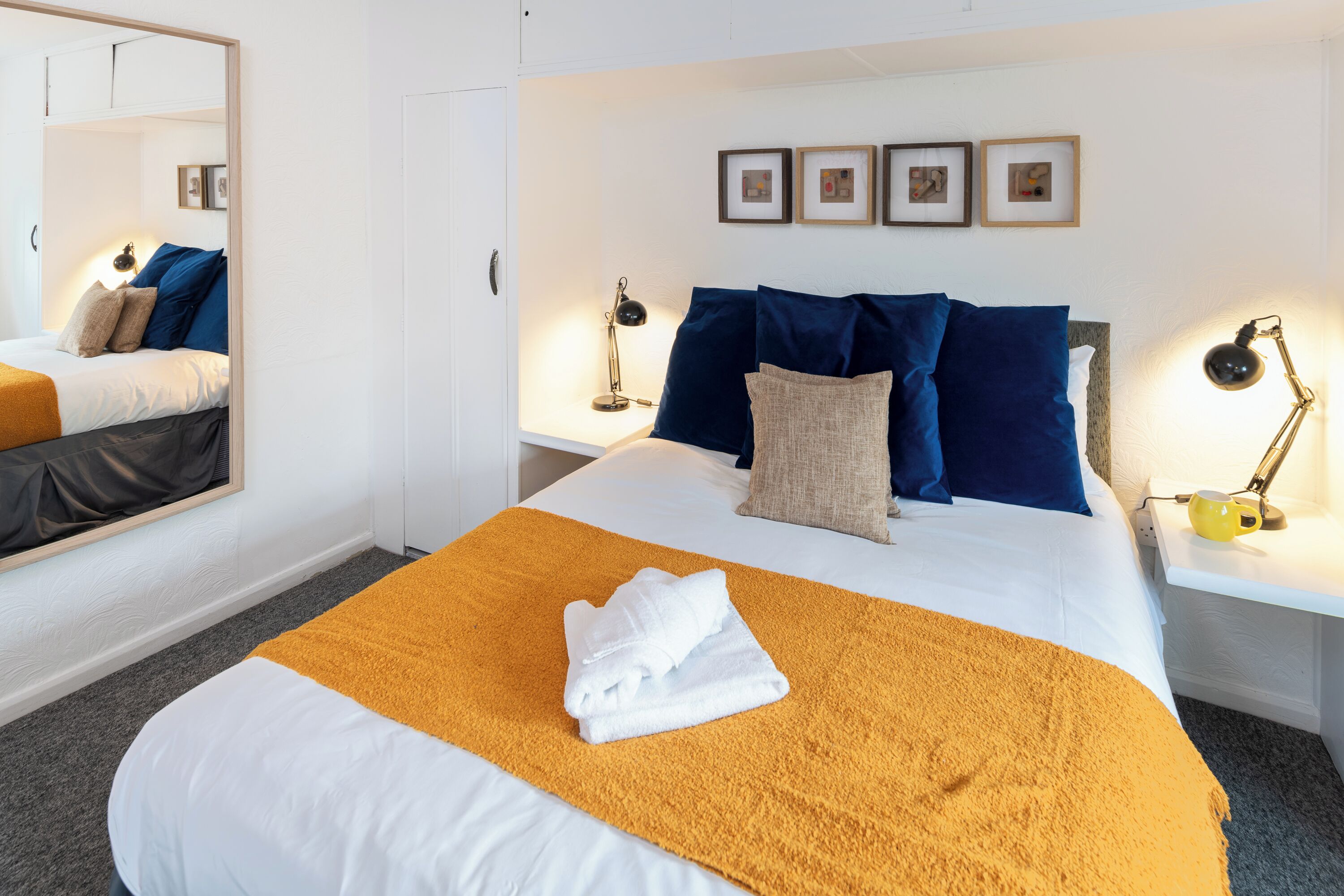 Quarto de hotel com uma cama bem arrumada, um espelho grande e quadros nas paredes.