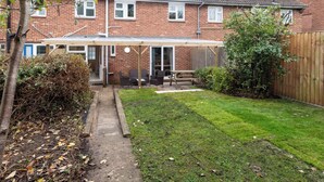 A two-story brick house with a covered patio, a lawn, and a wooden fence. - Terrace | Parking | Great for Couples | Sleeps 7 (Bristol)