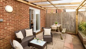 A patio with wicker furniture, a table set for two, and a wooden fence. - Terrace | Parking | Great for Couples | Sleeps 7 (Bristol)