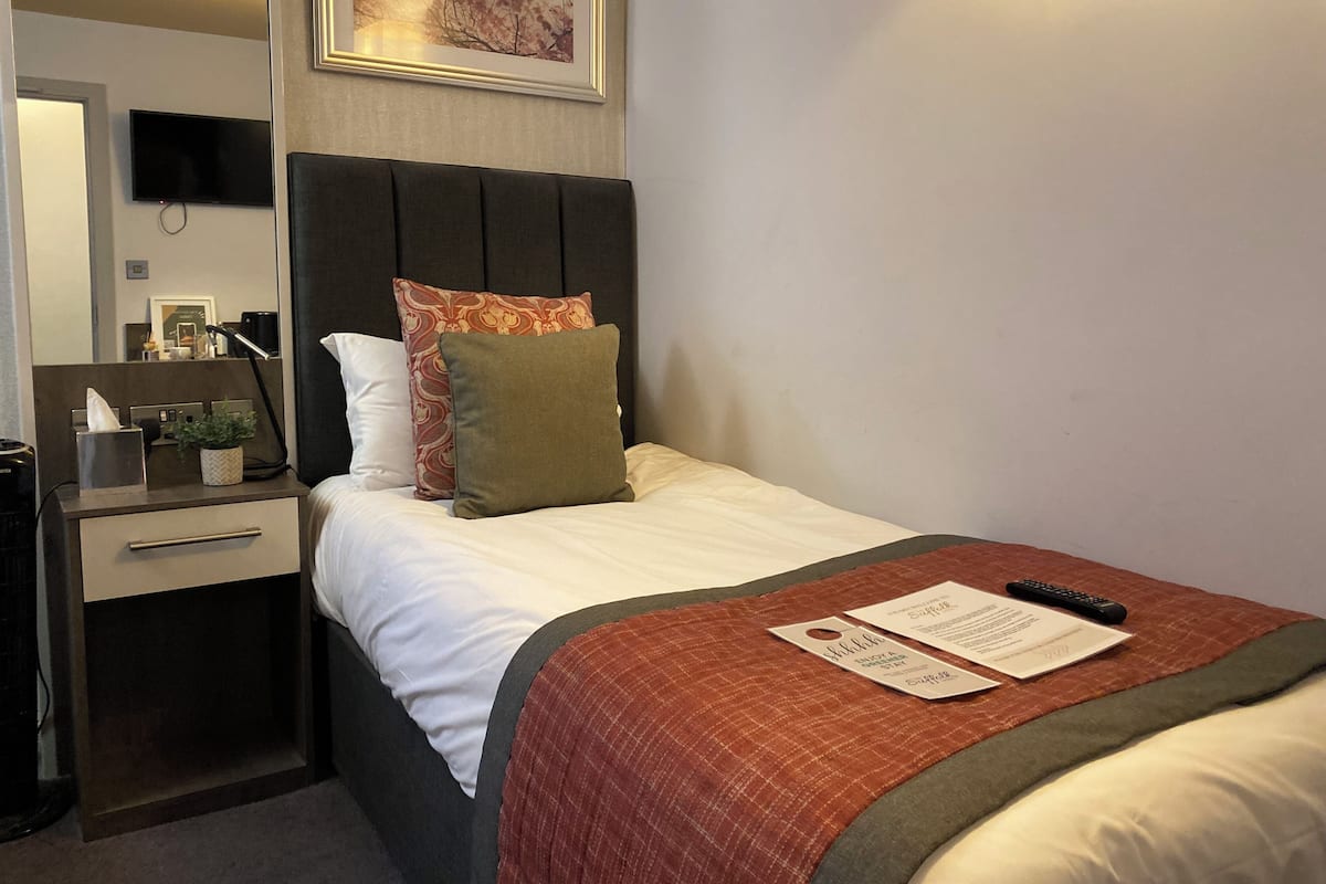 A hotel room with a bed, a bedside table with a lamp, a TV, and a framed picture on the wall.