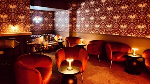A dimly lit lounge area with patterned wallpaper, leather seating, and small tables with lamps. - The Suffolk Hotel (Haverhill)