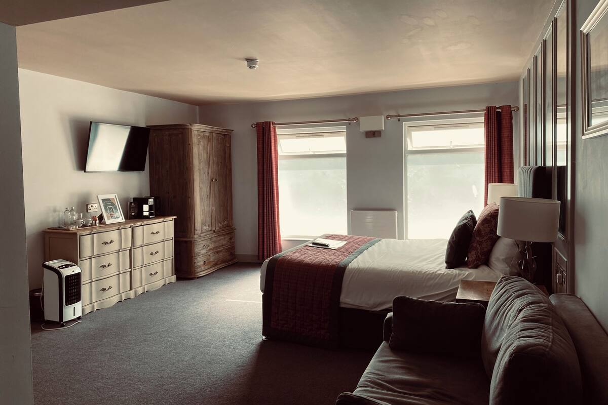 A bedroom with a bed, a wardrobe, a desk, a television, and a window.