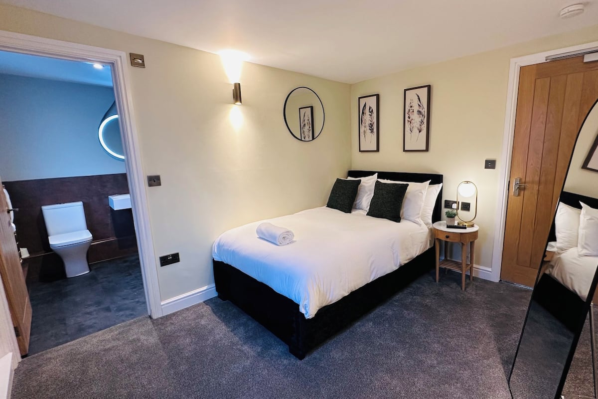 A hotel room with a bed, bedside table, wall art, and a mirror.