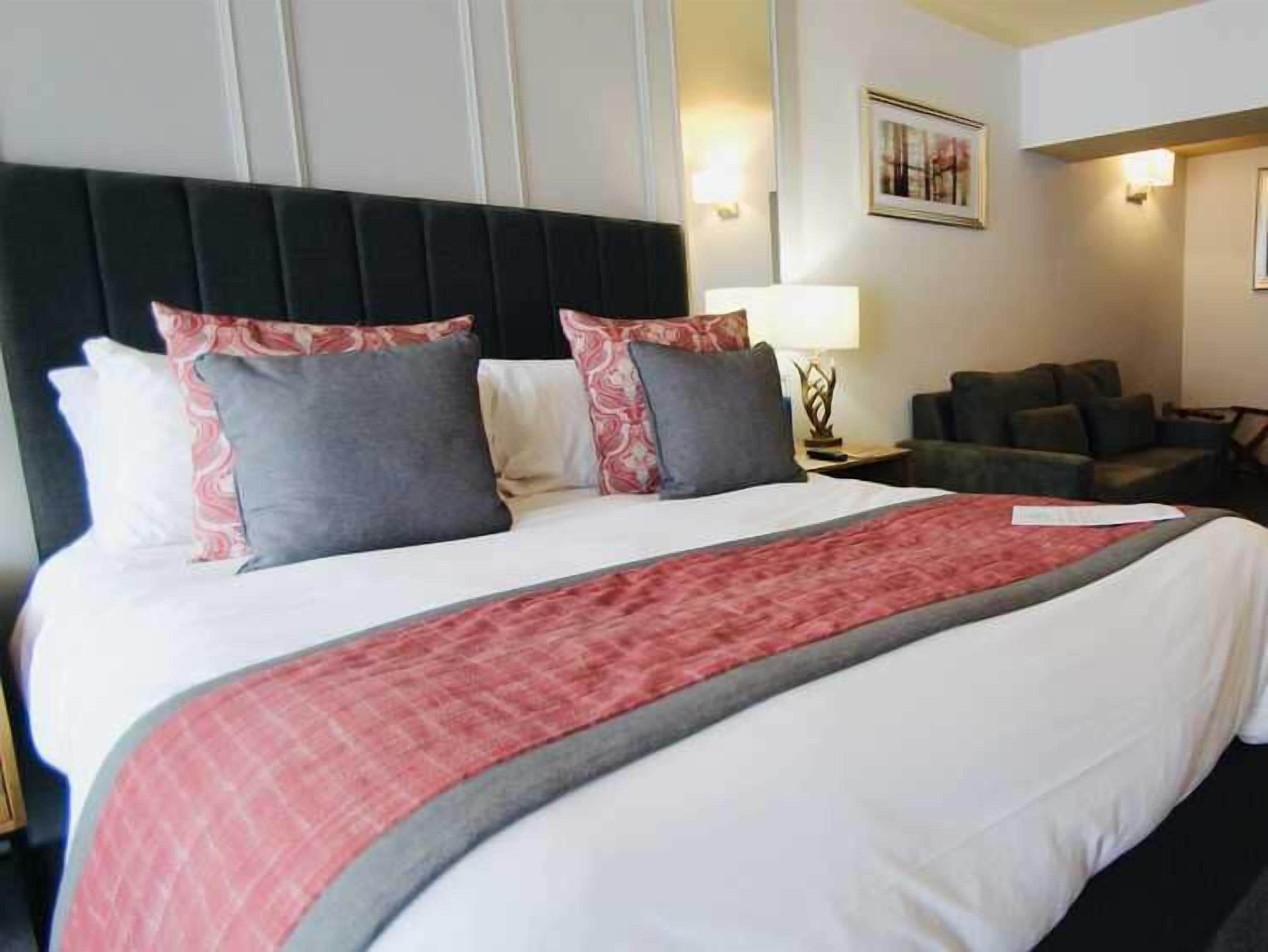 Una habitación de hotel con una cama grande, cabecera negra y sofá gris.