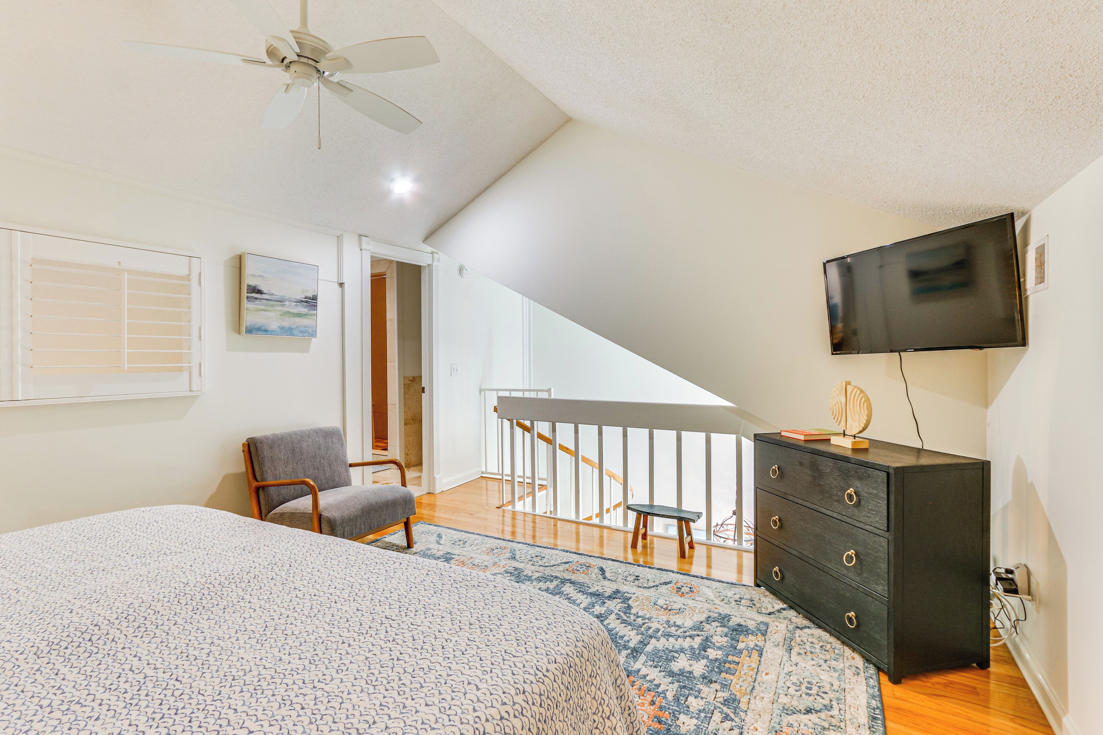 A bedroom with a bed, a chair, a dresser, a TV, and a staircase.