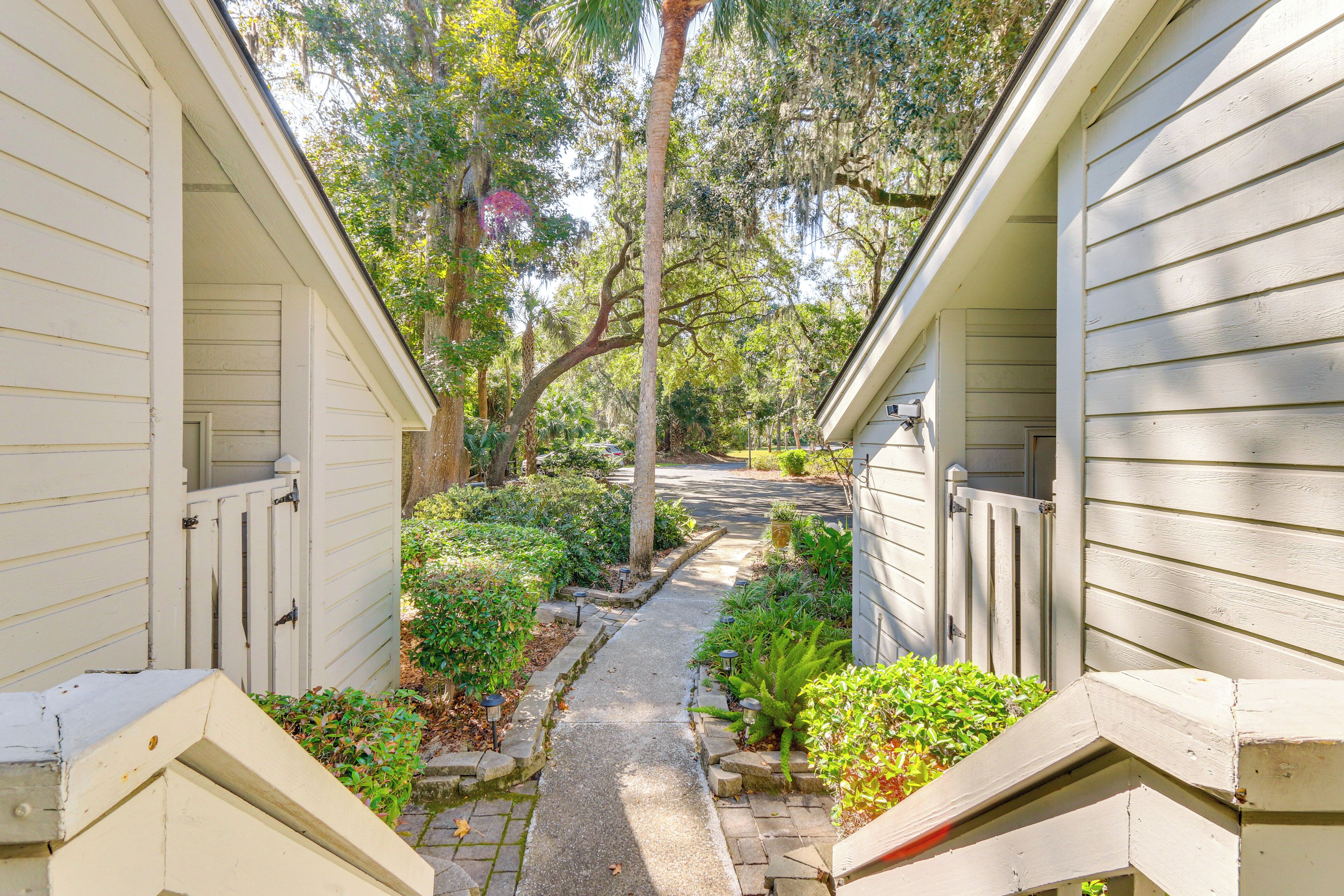 A pathway leading to a house with a covered porch, surrounded by lush greenery and trees.