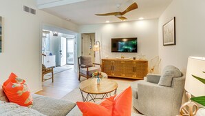 A modern living room with a ceiling fan, a flat-screen TV, and a dining area with a wooden cabinet.