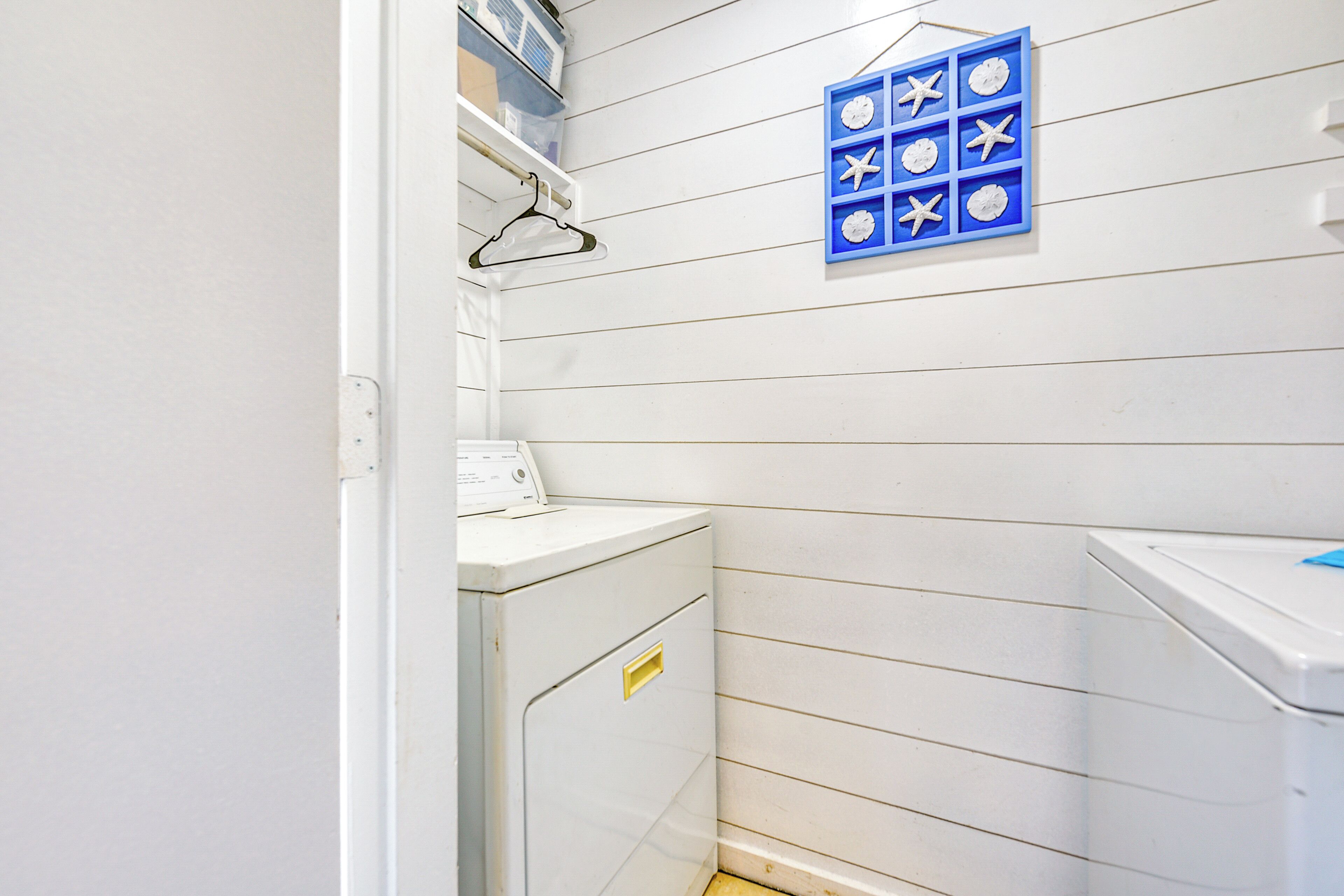 A laundry room with white walls, a blue wall-mounted clock, and a white washing machine.