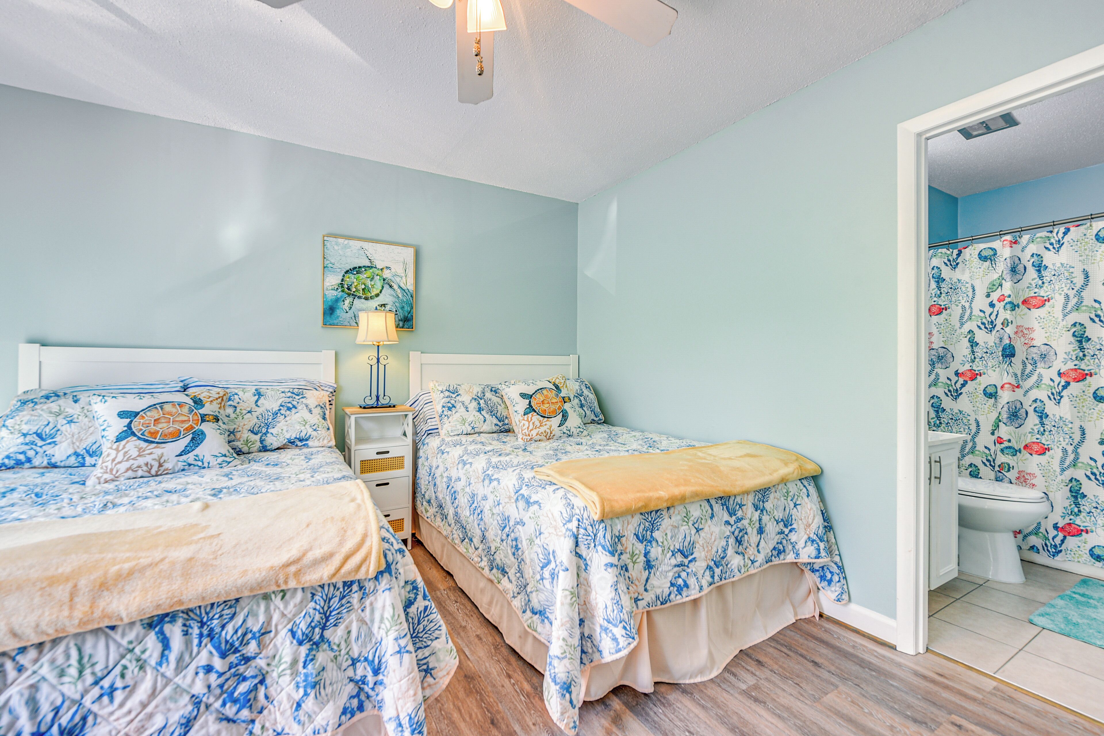 A bedroom with two beds, a nightstand, a lamp, and a bathroom with a toilet and shower.
