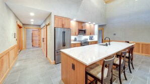 A modern kitchen with a large island, wooden cabinets, stainless steel appliances, and a tiled floor.