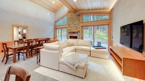 A spacious living room with a large sectional sofa, a wooden dining table, and a stone fireplace.