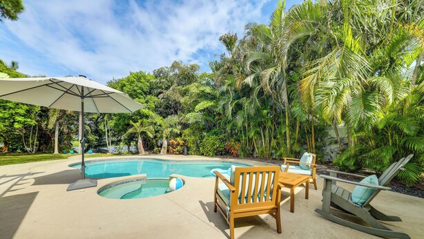 A pool area with a wooden deck, lounge chairs, and a large umbrella. - Tropical Pool Oasis on 1/4 Acre by Downtown Stuart (Stuart)