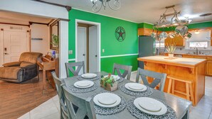 A dining area with a table set for six, a kitchen with hanging pots, and a green accent wall. - Cozy Home W/fire Pit: Drive to Palo Duro Canyon! (Amarillo)
