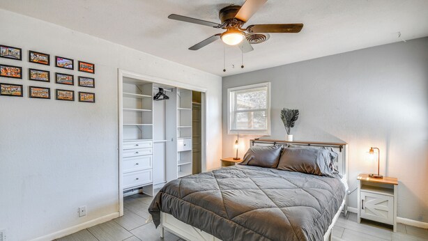 A bedroom with a bed, a ceiling fan, a nightstand with a lamp, a window with blinds, and a closet with hanging items. - Cozy Home W/fire Pit: Drive to Palo Duro Canyon! (Amarillo)
