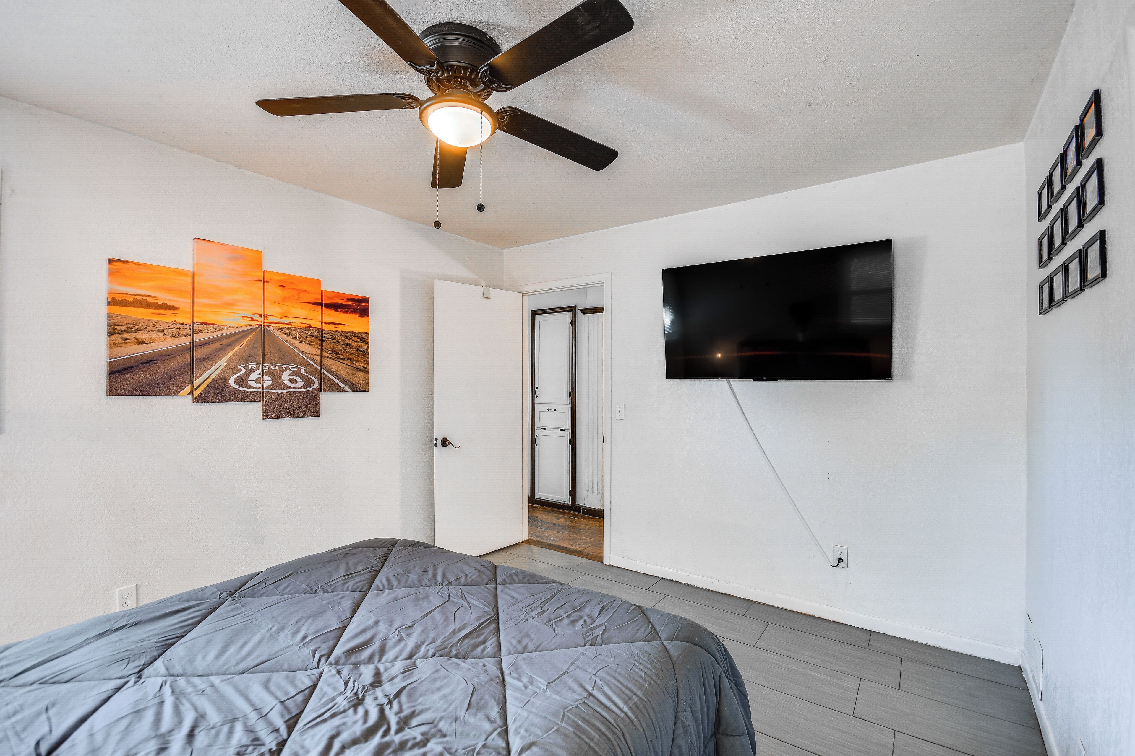 Ein Schlafzimmer mit einem Bett, einem Deckenventilator, einem an der Wand montierten Fernseher und einer Tür zu einem anderen Raum.