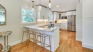 A modern kitchen with white cabinetry, stainless steel appliances, and a central island with bar stools. - Lake Keowee Home w/ Boat Dock in Seneca (Seneca)
