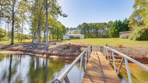 A wooden dock leading to a white building with a covered area, surrounded by trees and a body of water. - Lake Keowee Home w/ Boat Dock in Seneca (Seneca)