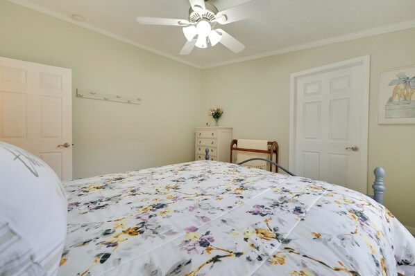 A bedroom with a floral bedspread, a ceiling fan, a dresser, and a door with a picture on the wall.