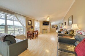 A spacious living room with a dining area, a sofa, a TV, and a view through large windows.