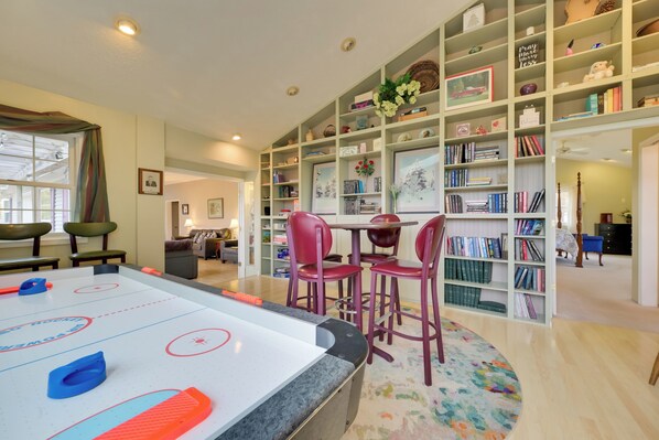 A cozy room with a pool table, a bookshelf, and a dining area with chairs.