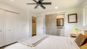 Une chambre à coucher comprenant un lit, un ventilateur de plafond, une table de chevet avec une lampe, un miroir et une porte coulissante.