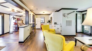 Eine moderne Küche mit weißen Schränken, einer Mikrowelle und einer an der Wand hängenden Gitarre. Im Wohnbereich befindet sich ein gelber Sessel und ein Sofa mit Karomuster.